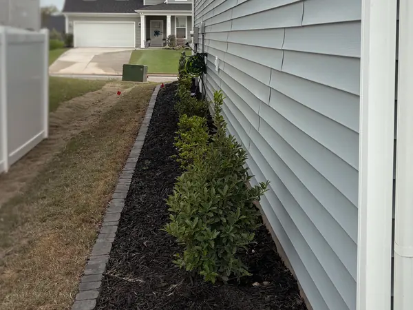 A narrow mulch bed with a brick border running the length of a house.