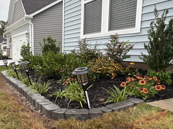 A stone-bordered bed with flowering plants and landscape lighting.